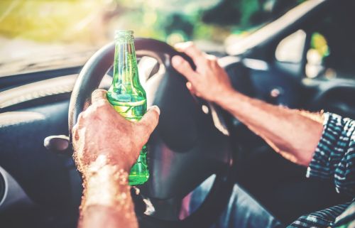 A man drinks beer while driving a car. Concept for understanding the Georgia open container law.