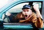 A angry man driving a car yells and shakes his fist through the car window demonstrating aggressive driving.