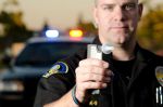 A police officer holds a breath test machine in his hand ready at a traffic stop with his patrol car in the background.*the officer was blurred on purpose to place focus on the mouth piece. Concept for What Is the Legal Limit for DUI in Georgia?
